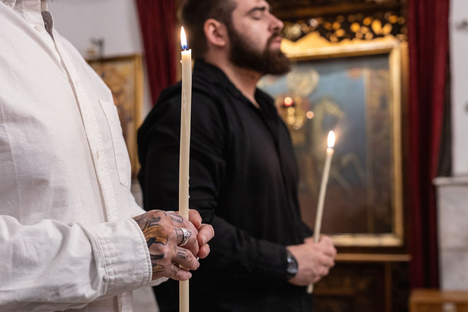 Two men holding candles during an Orthodox Christian church service ceremony.