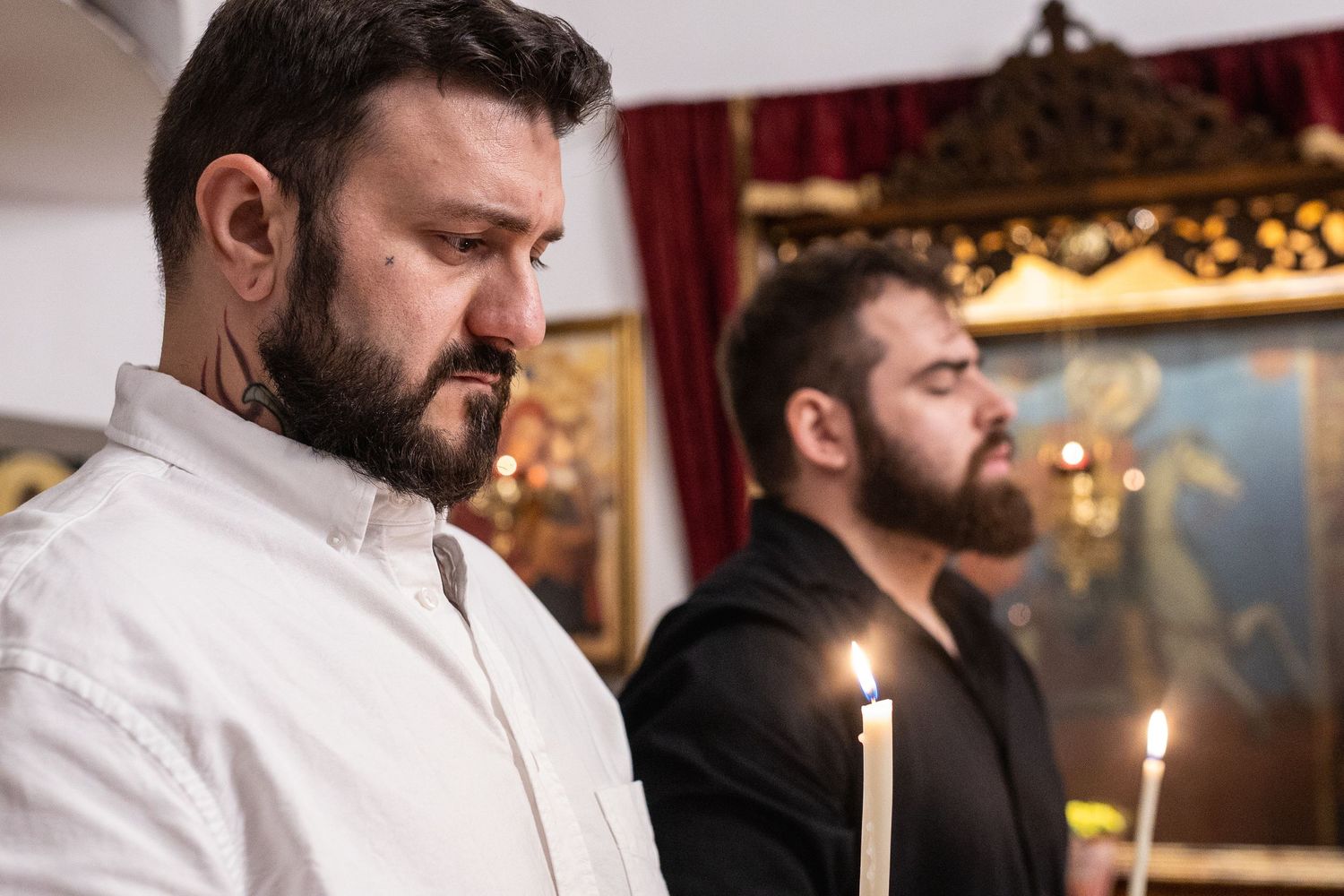 Two bearded men holding candles in an Orthodox church during a religious ceremony.