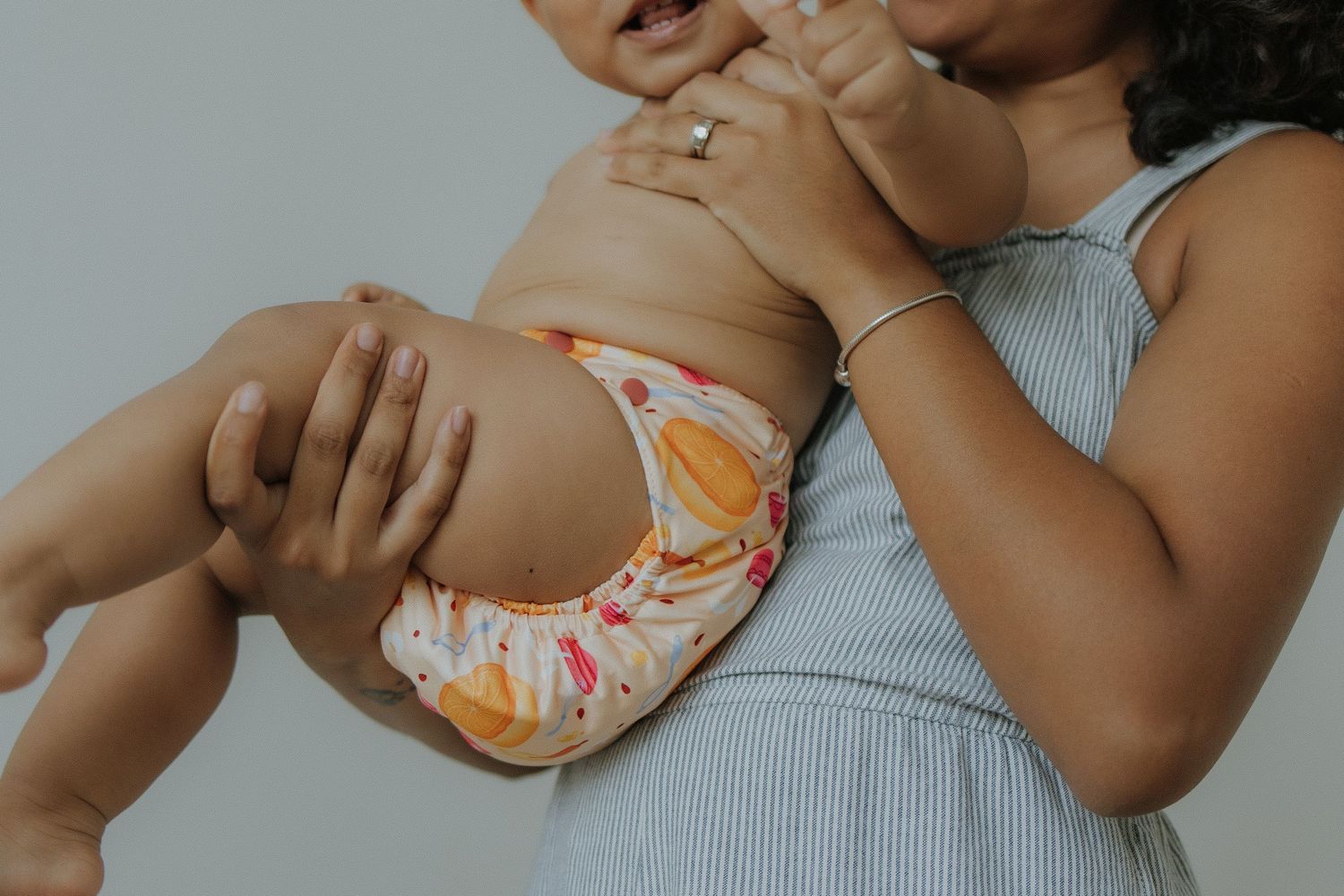 Mother holding baby wearing colorful cloth diaper, showcasing reusable eco-friendly diapering solution.