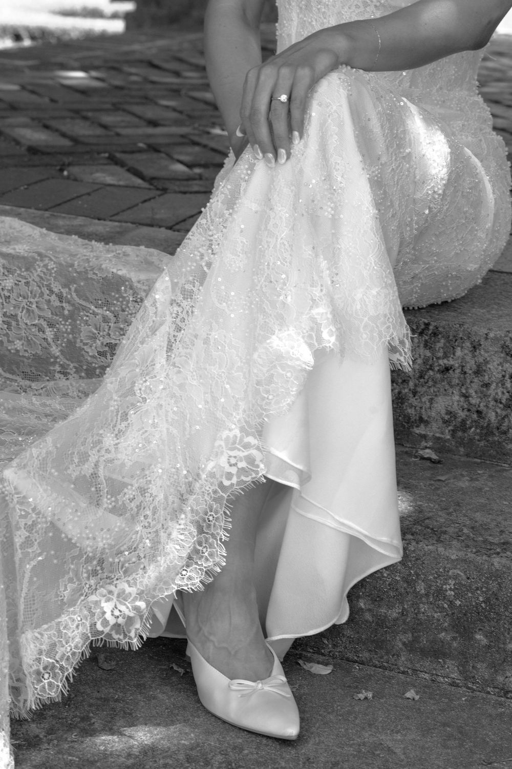 Close-up of bride in lace wedding gown adjusting her dress hem, wearing white satin ballet flats.