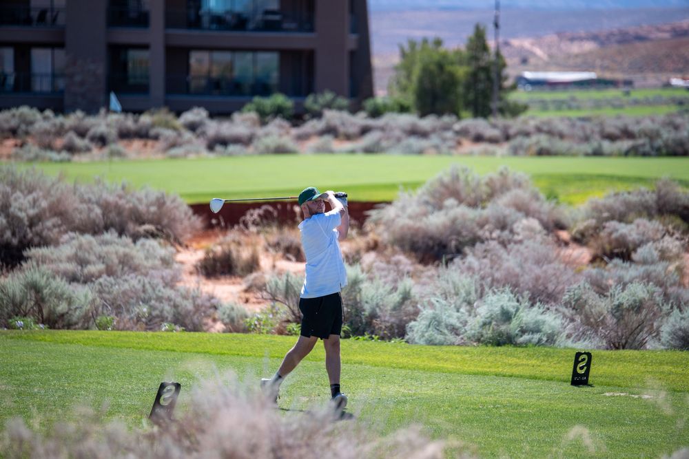 Golfer mid-swing on a desert golf course with red rock landscape and sagebrush in St. George, Utah.