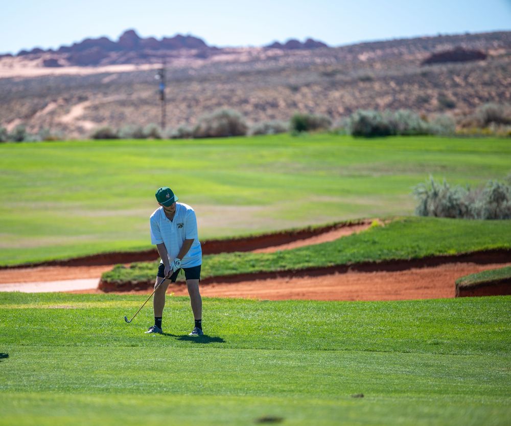 Golfer preparing to chip onto a green at a desert golf course with red rock formations in the background.