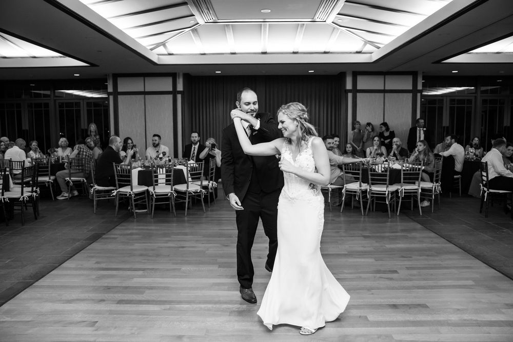 Bride and groom share their first dance at wedding reception in elegant ballroom with guests watching.