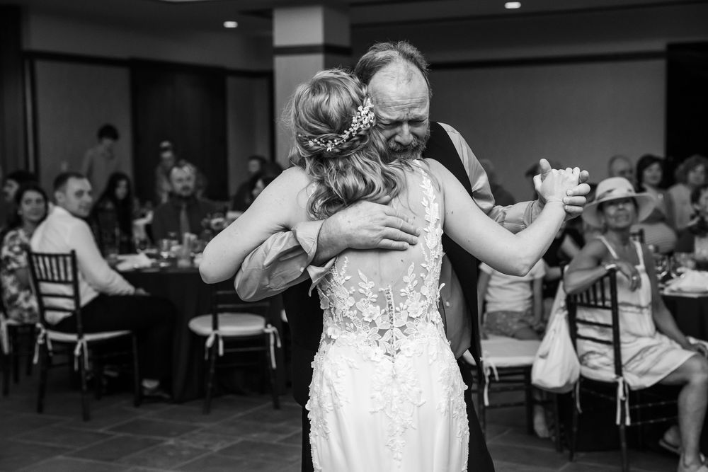 Bride and father share an emotional first dance embrace at wedding reception in black and white photo.