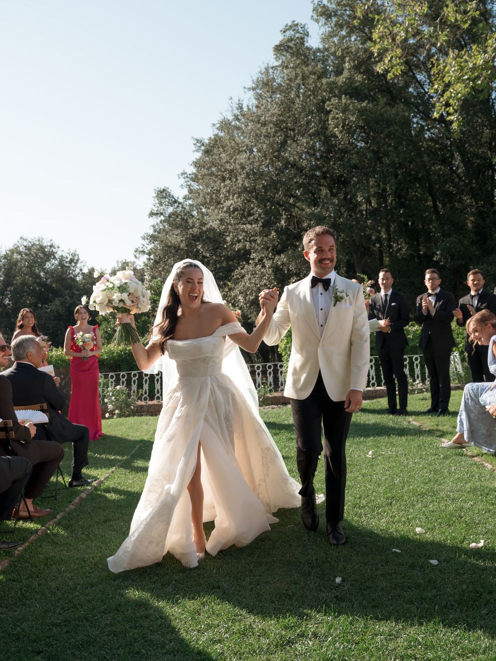 Bride and groom walk down the aisle at an outdoor wedding ceremony on a lush green lawn.