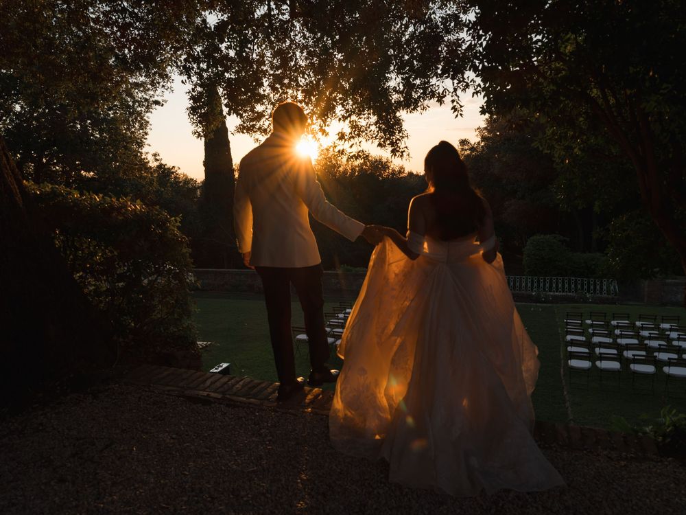 Silhouette of bride and groom walking at sunset through garden with golden light.
