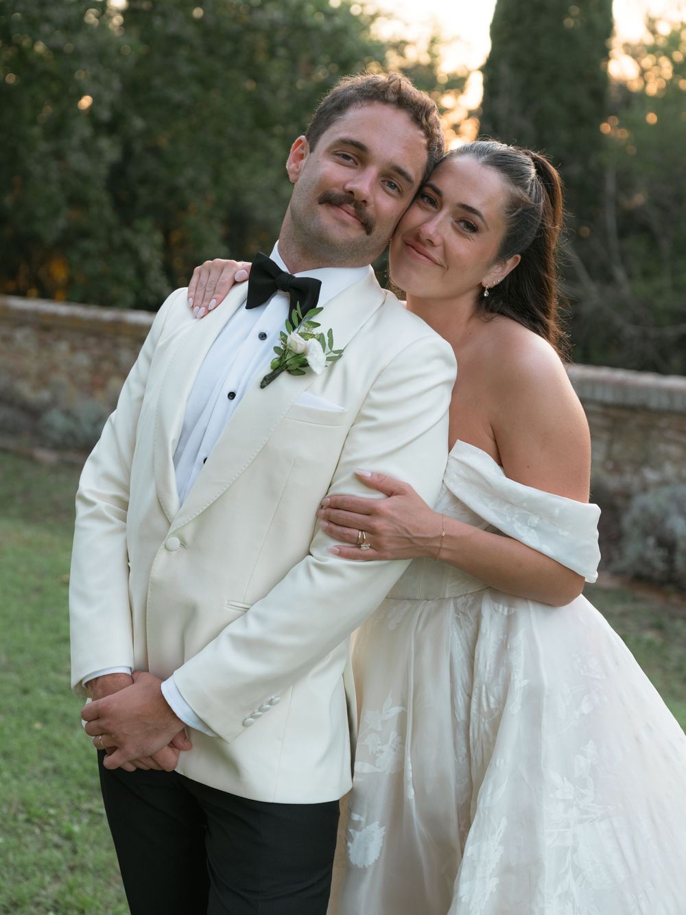 Happy couple in matching ivory wedding attire embrace outdoors at elegant Italian villa wedding.