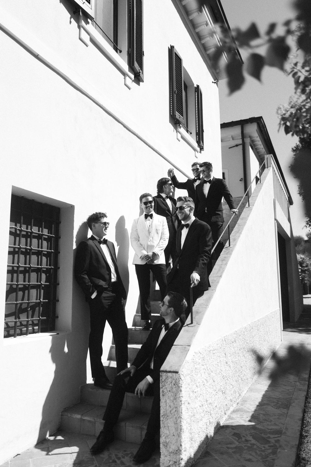 Black and white photo of groomsmen in tuxedos posing on outdoor staircase.