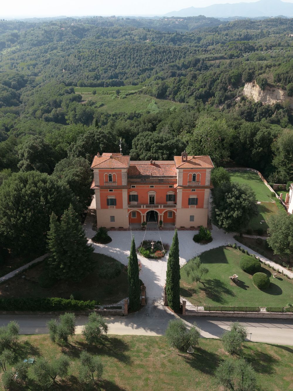 Aerial view of grand Italian villa with terracotta roof surrounded by lush Tuscan countryside.