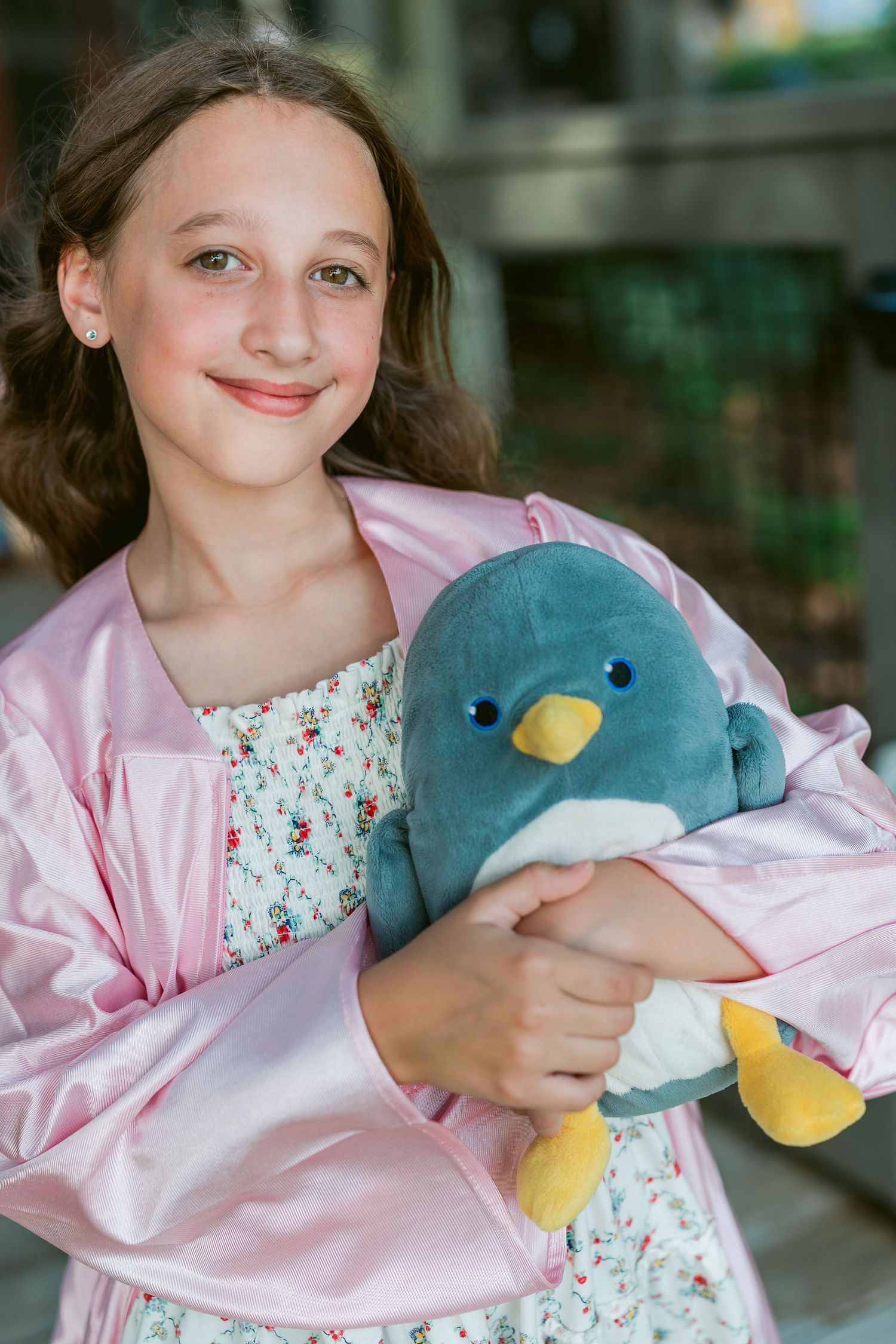 Young girl in pink graduation cap and gown with glitter cowboy boots sits smiling on wooden steps.