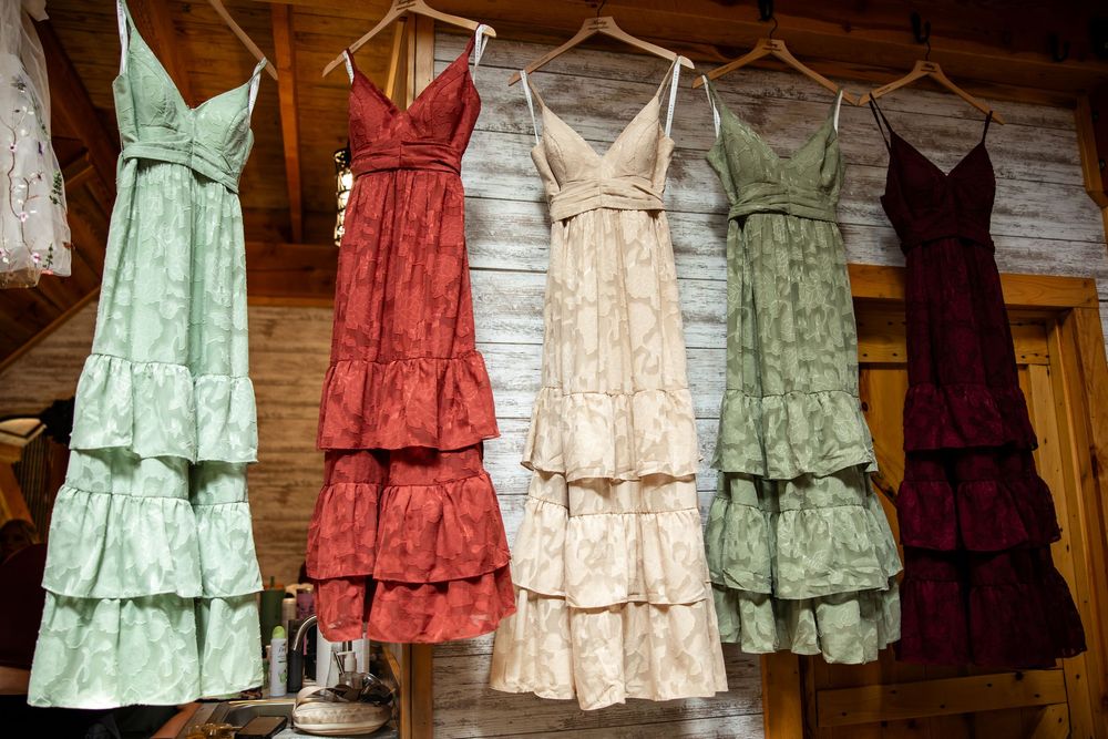 Four tiered spaghetti strap dresses in green, red, cream, and burgundy hanging on a rustic wooden wall display.