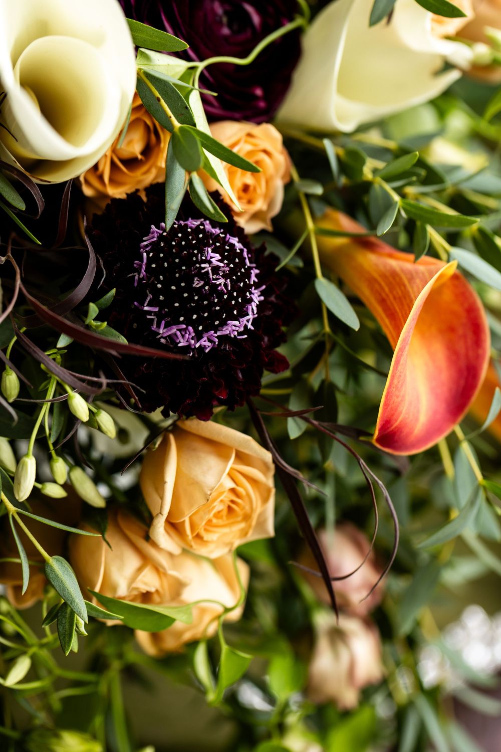 Elegant floral arrangement featuring peach roses, purple scabiosa, calla lilies, and lush greenery for a wedding bouquet.