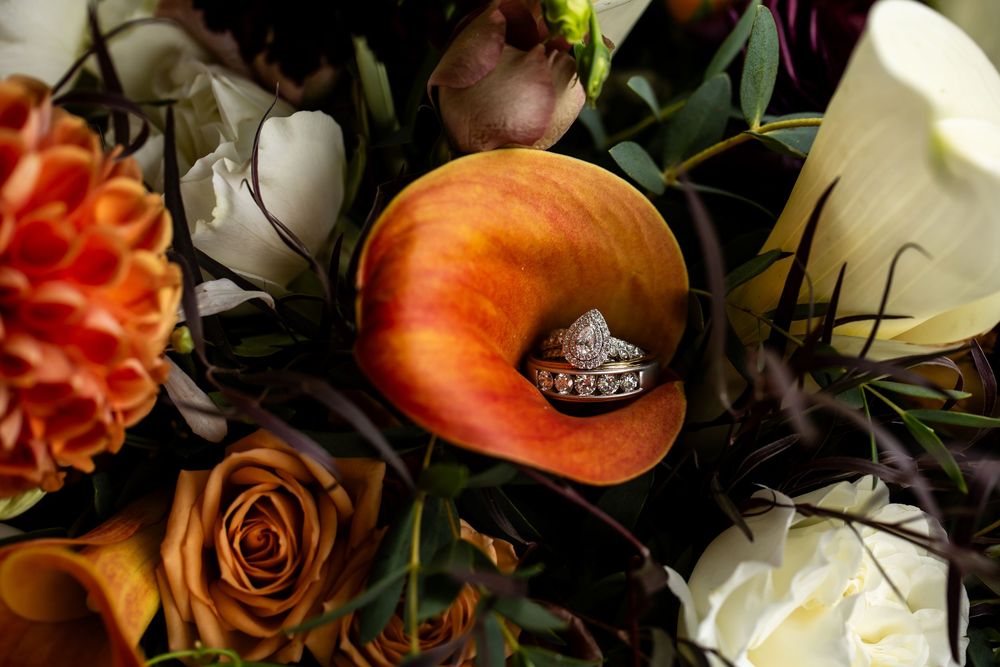 Diamond engagement ring nestled in an orange calla lily surrounded by roses and white flowers in a fall wedding bouquet.