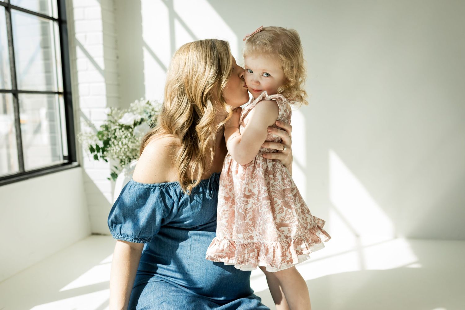 Expecting mother kisses young daughter's cheek during a Calgary motherhood studio photography session