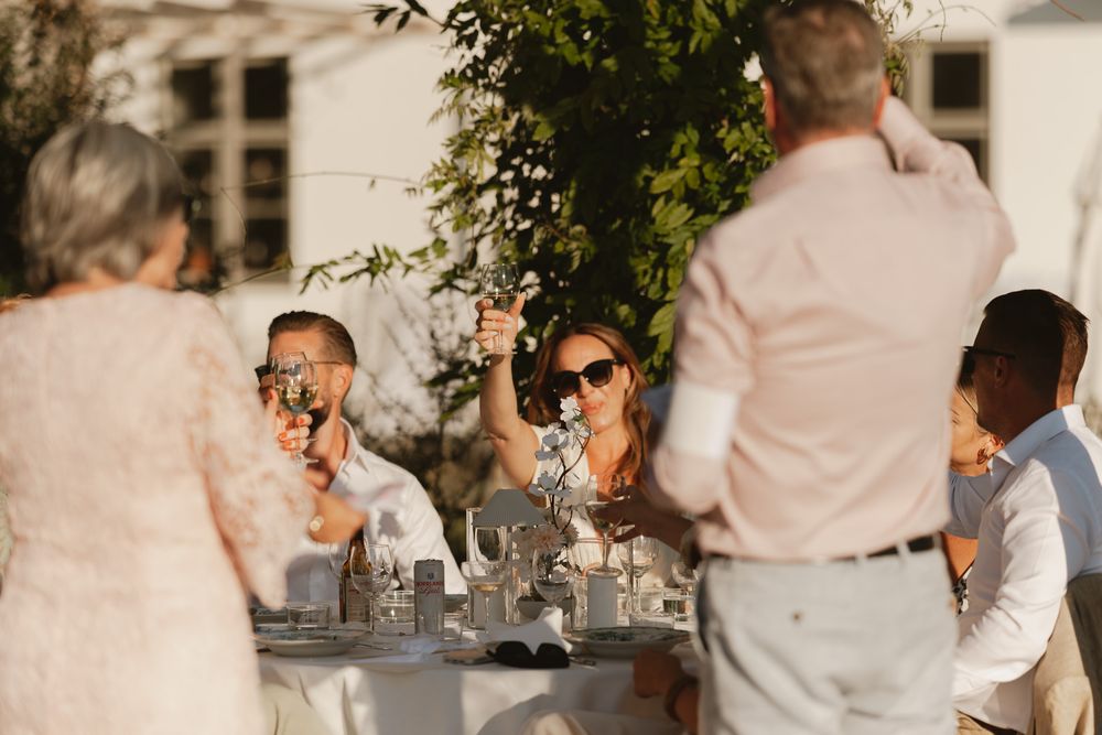 Guests raising glasses in a toast at an elegant outdoor wedding reception table in warm golden sunlight.