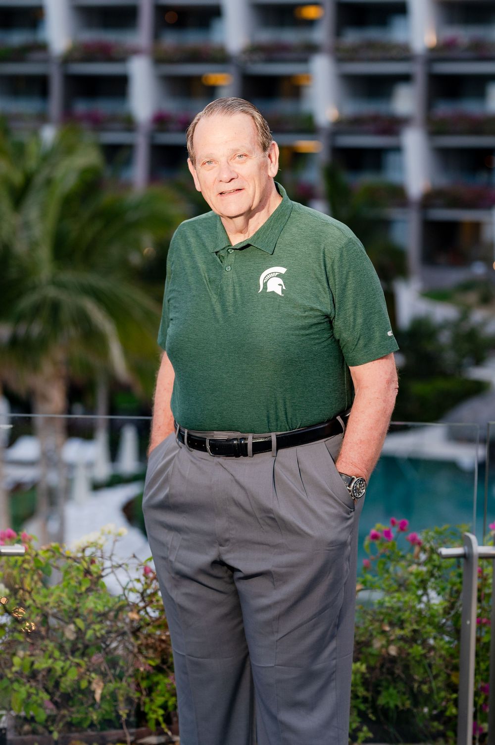 Older man in Michigan State green polo shirt standing at tropical resort pool area.