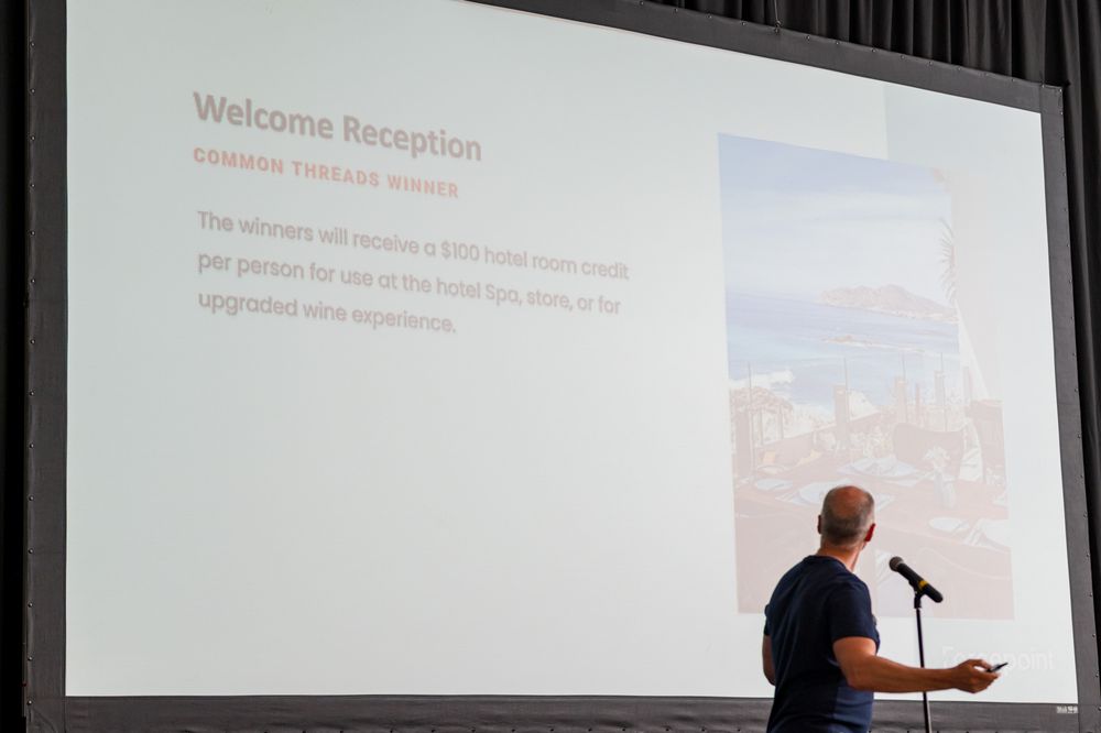 Speaker presenting Welcome Reception award slide on large screen at a conference event.