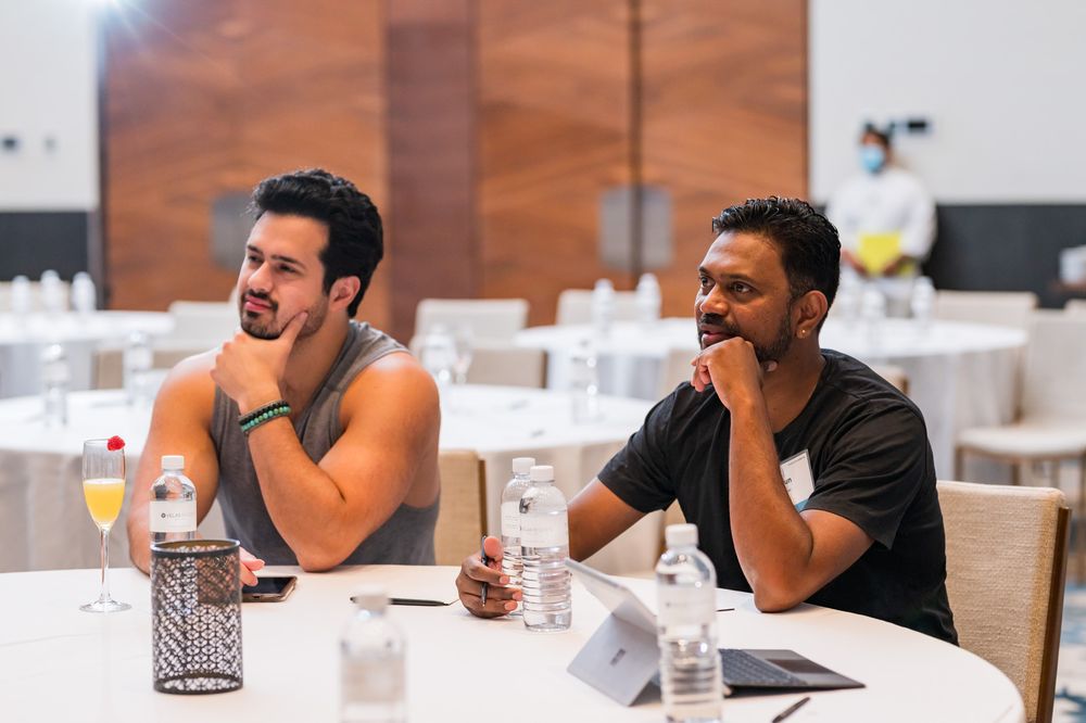 Two men sit at a round table in a conference room, listening attentively during a business meeting or workshop.
