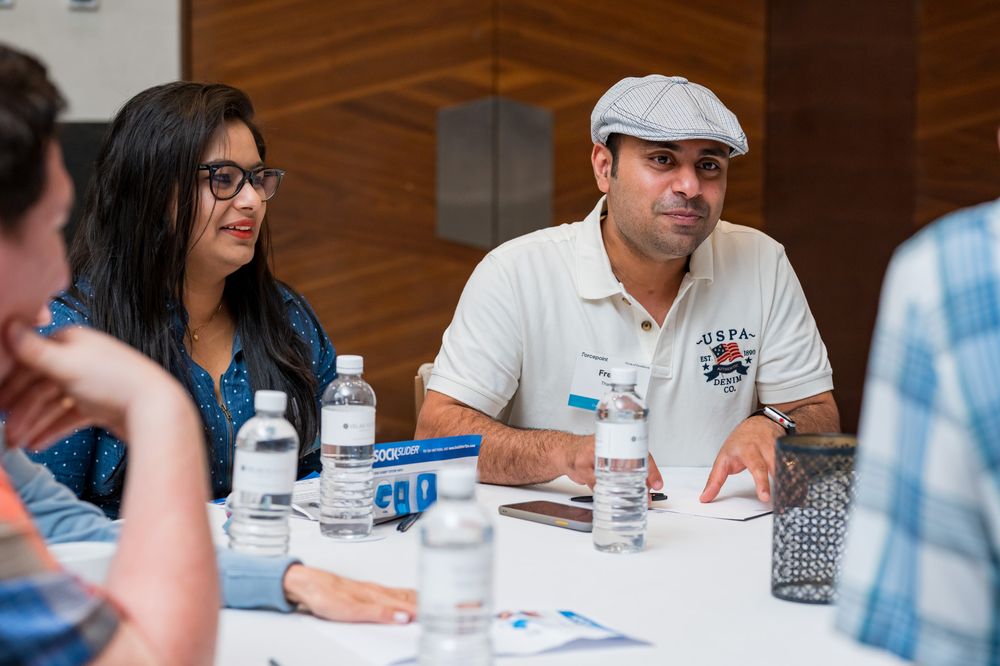 Two professionals engage in a discussion at a conference table with water bottles and documents.
