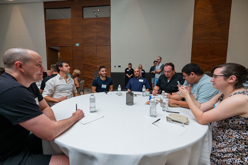 Professionals engaged in a business discussion seated around a round white table in a modern conference room.
