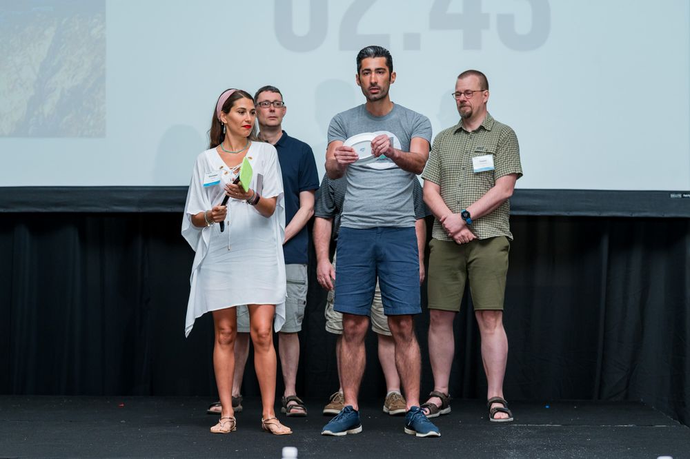 Four people standing on stage in front of a projection screen during a presentation event.
