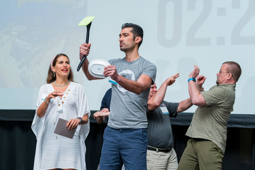 Three people on stage at a conference, one holding a yellow marker aloft near a timer display.
