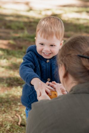 Smiling toddler in blue knit sweater reaching out to adult outdoors in sunny park in Rouse Hill.