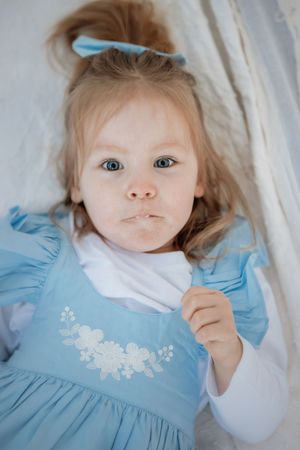 Adorable toddler girl with blue eyes in a light blue floral dress and matching bow, making a pouty face in a park in Kellyville.