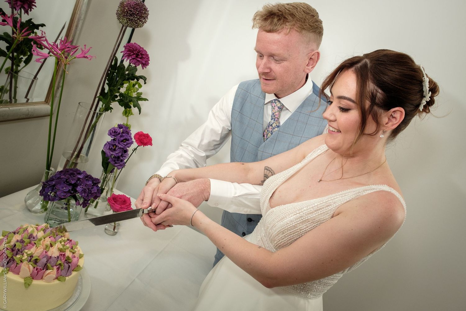 Bride and groom cutting their wedding cake together, surrounded by colorful floral arrangements.