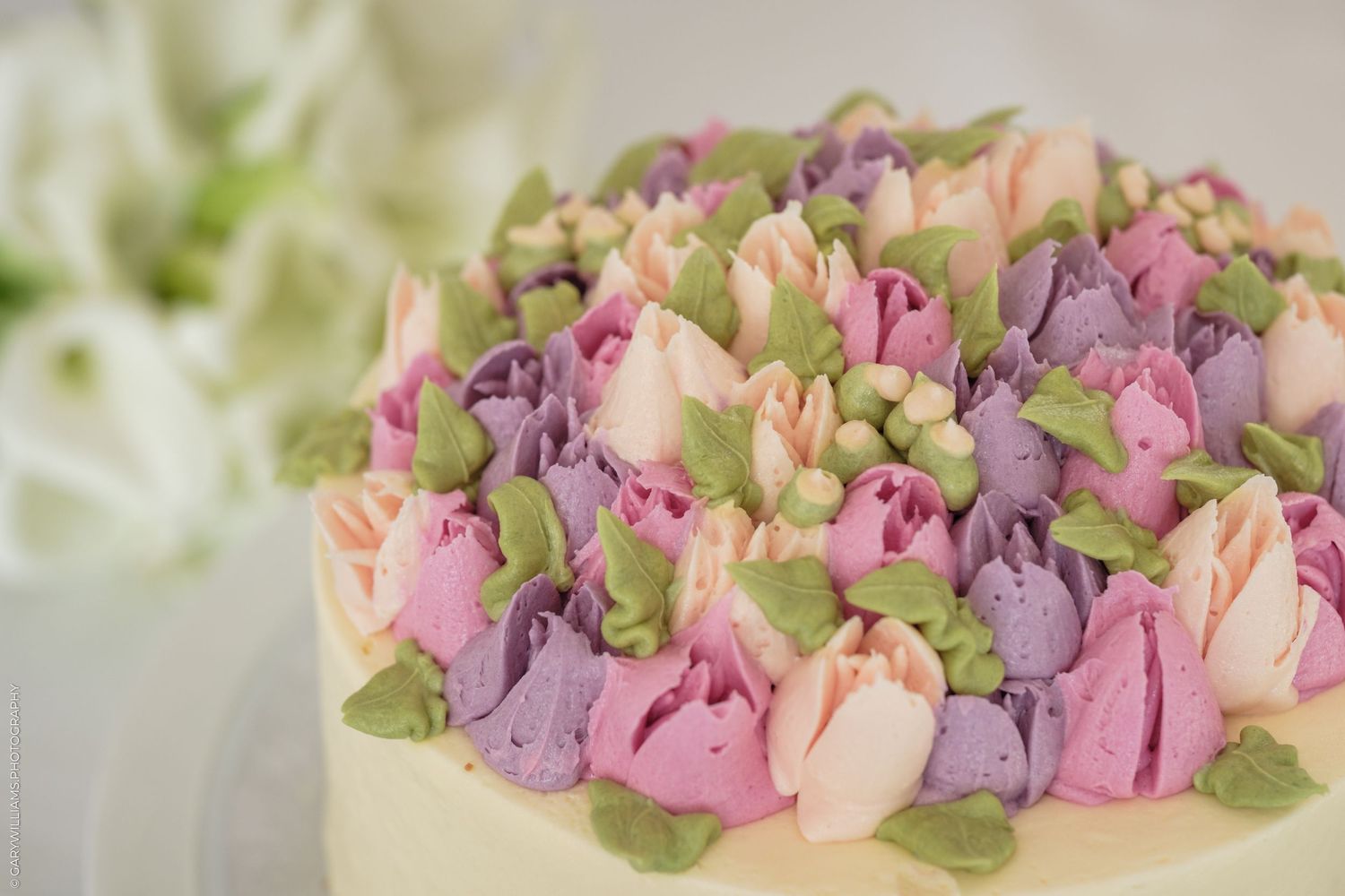 Elegant cake topped with pastel pink, purple frosting flowers and green leaves for a beautiful floral arrangement.