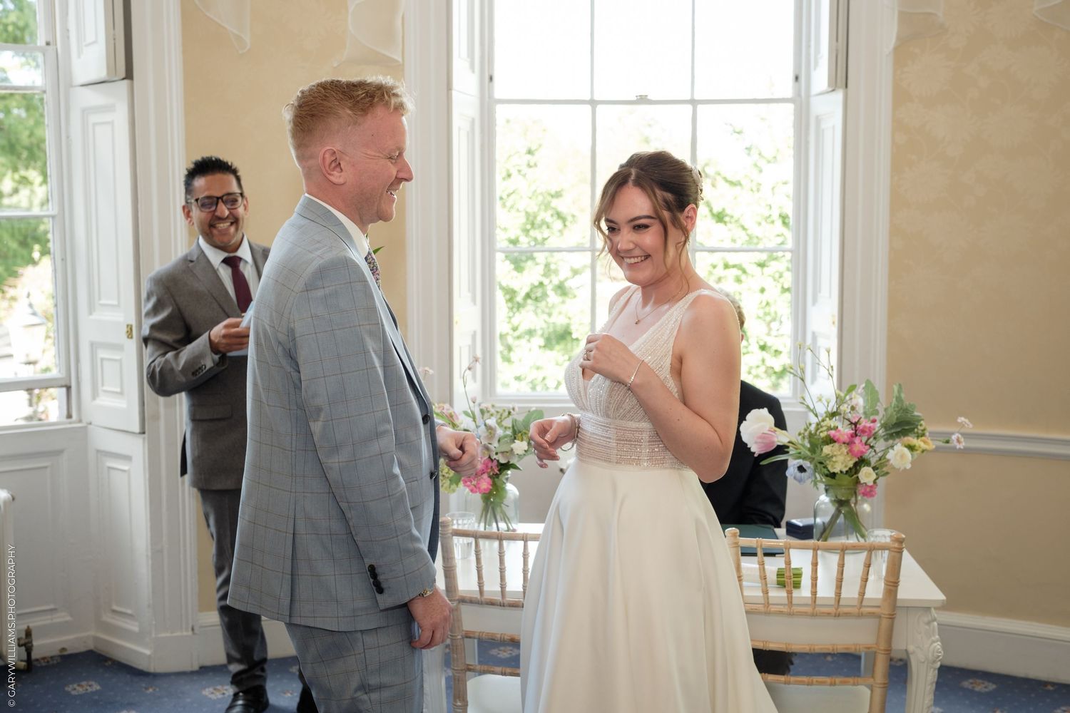 Bride and groom exchanging vows during an elegant indoor wedding ceremony with floral arrangements.