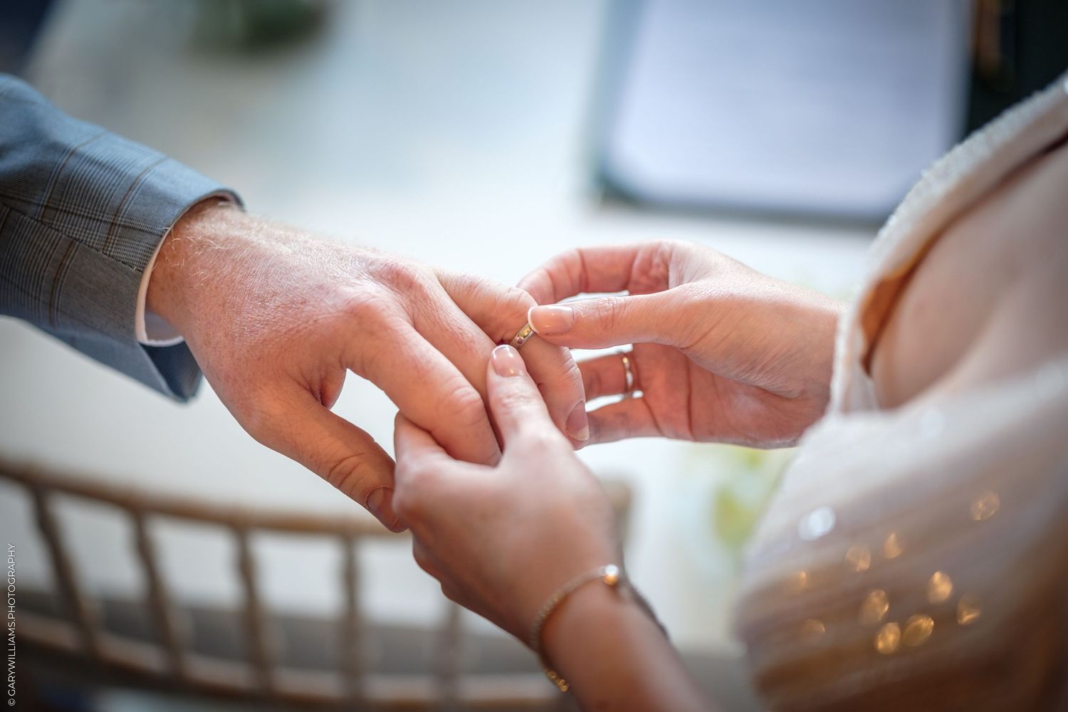 Close-up of a groom placing a gold wedding ring on the bride's finger during a wedding ceremony.