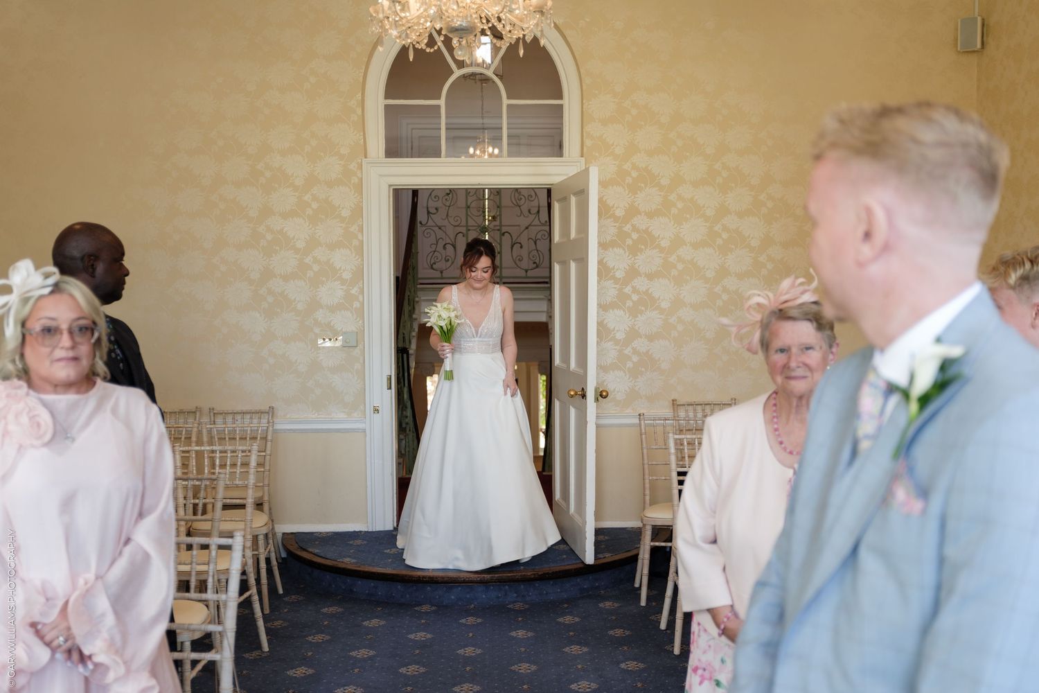 Bride in white gown walks down aisle toward groom at elegant wedding ceremony in a decorated venue.
