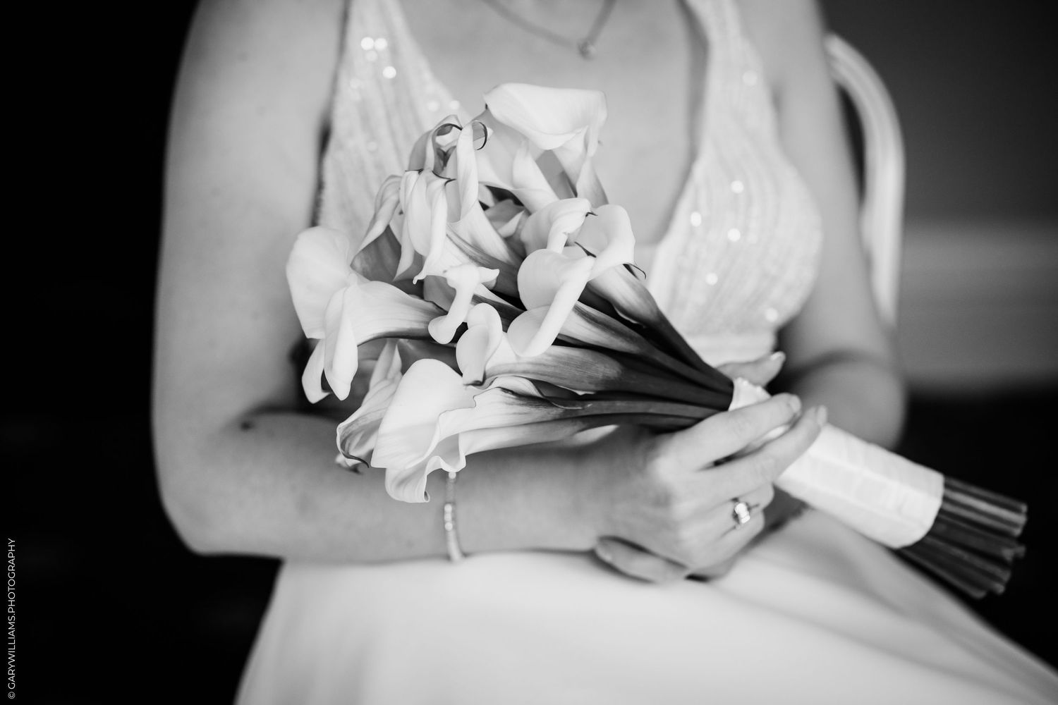 Bride holding elegant calla lily wedding bouquet in black and white photo, wearing a beaded gown and diamond bracelet.