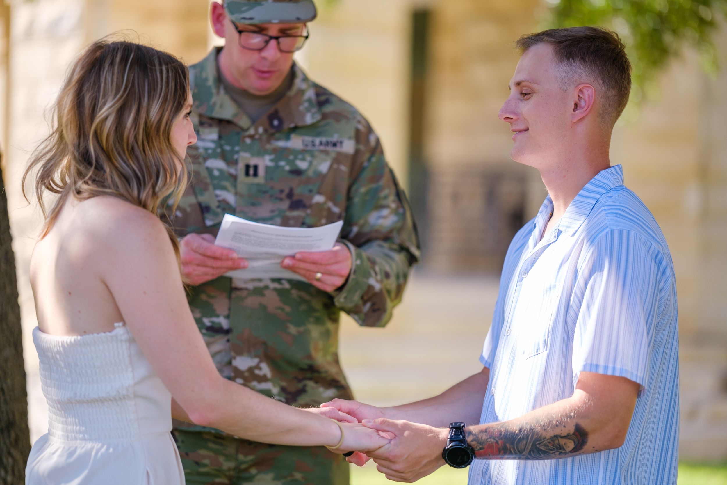 Couple holds hands during outdoor wedding ceremony officiated by a military officer in camouflage  in downtown Belton Texas