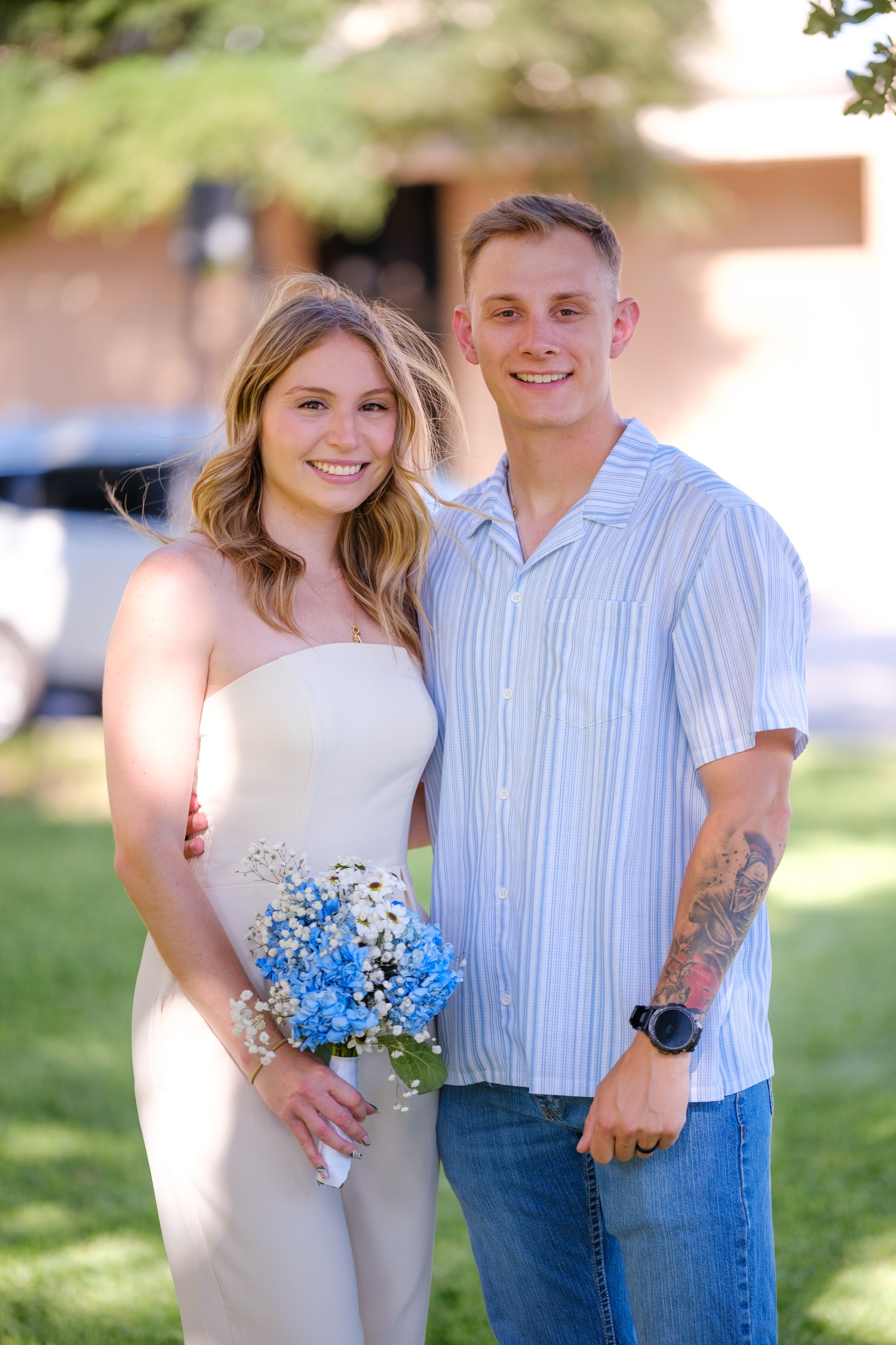 Smiling newlywed couple poses outdoors with bride holding a blue and white wildflower bouquet  in downtown Belton Texas