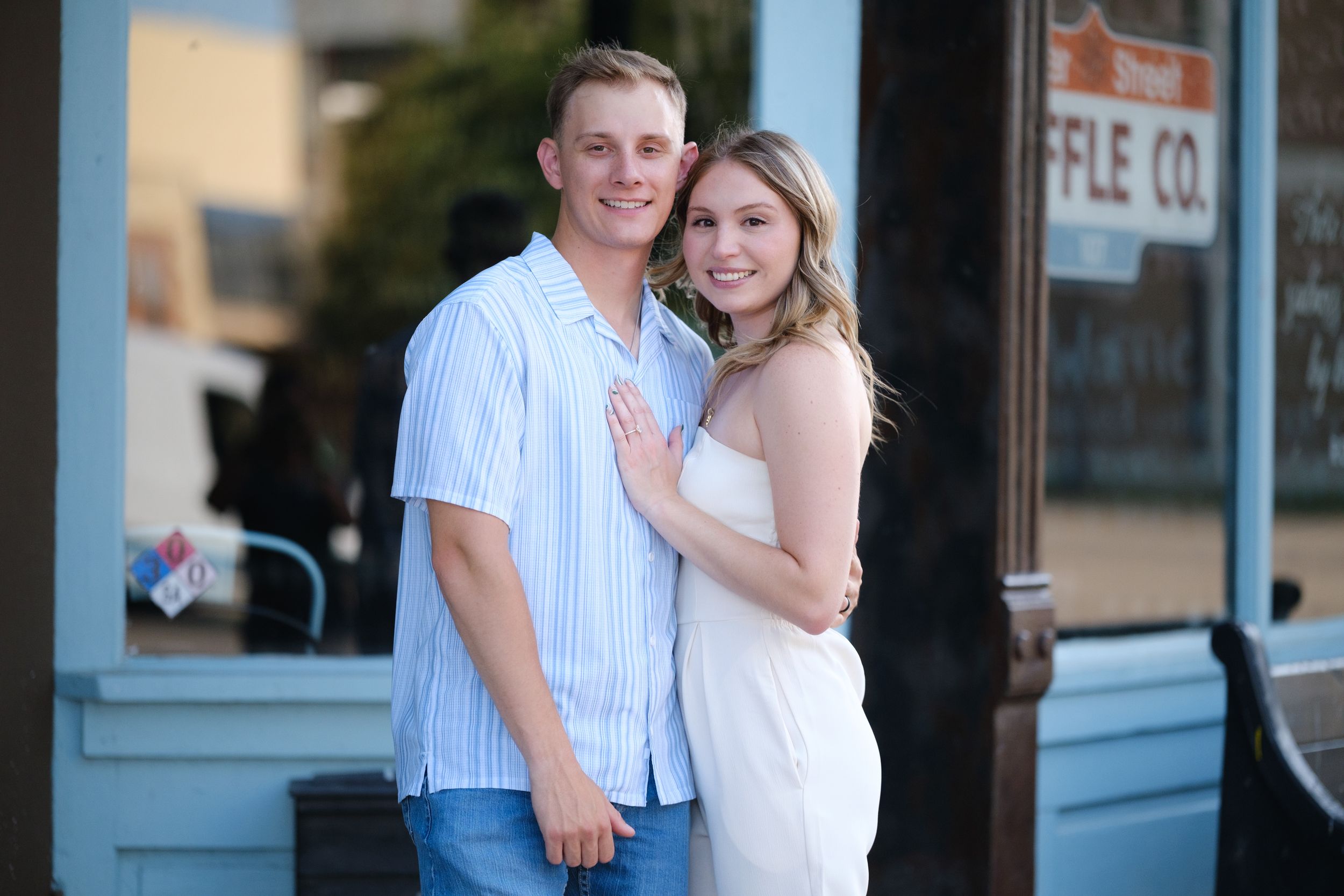 Happy couple embraces and smiles together outside a blue downtown storefront on a sunny day for wedding in downtown Belton Texas