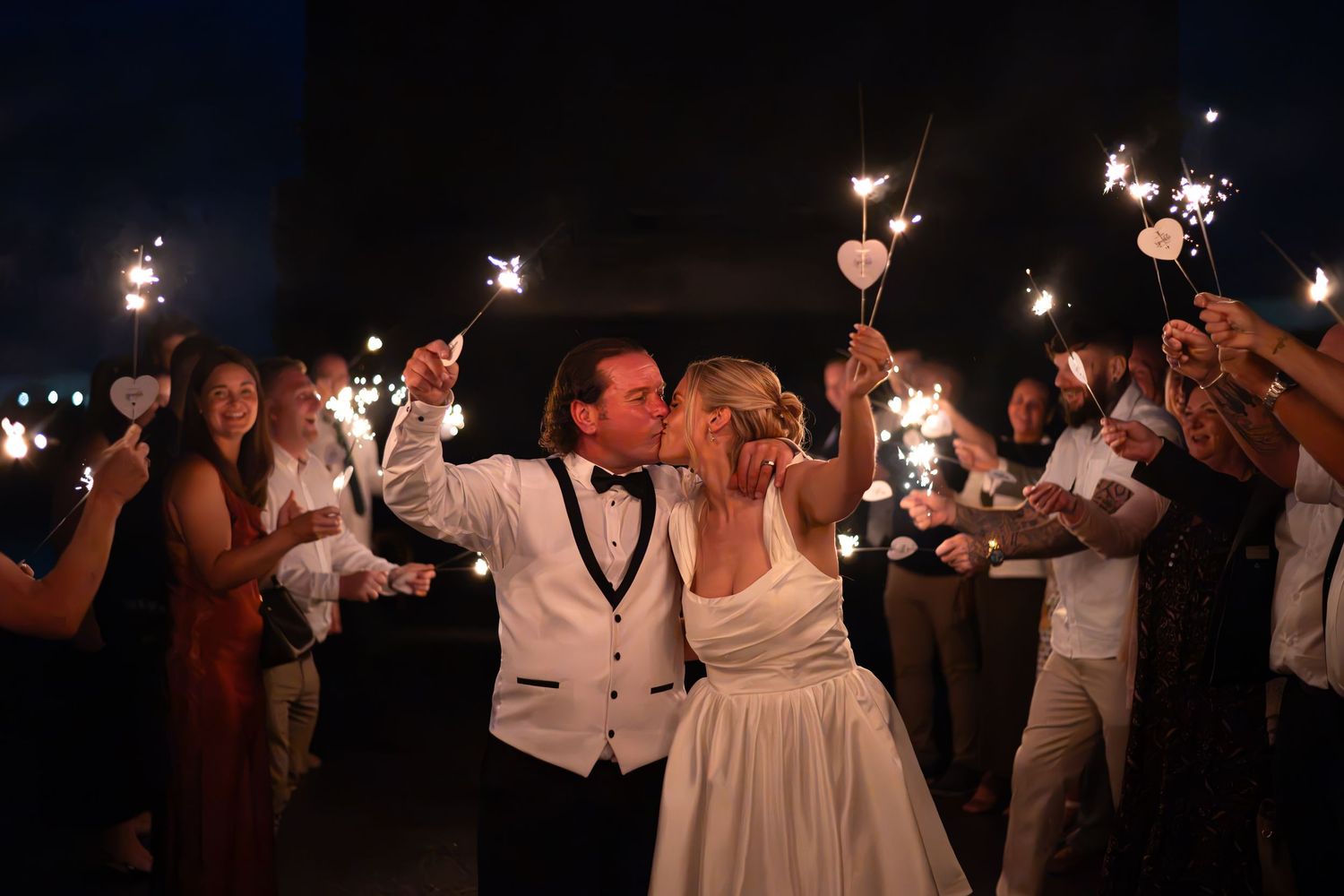 Bride and groom kiss during sparkler send-off at night wedding celebration with guests holding sparklers. Leeds Wedding day UK
