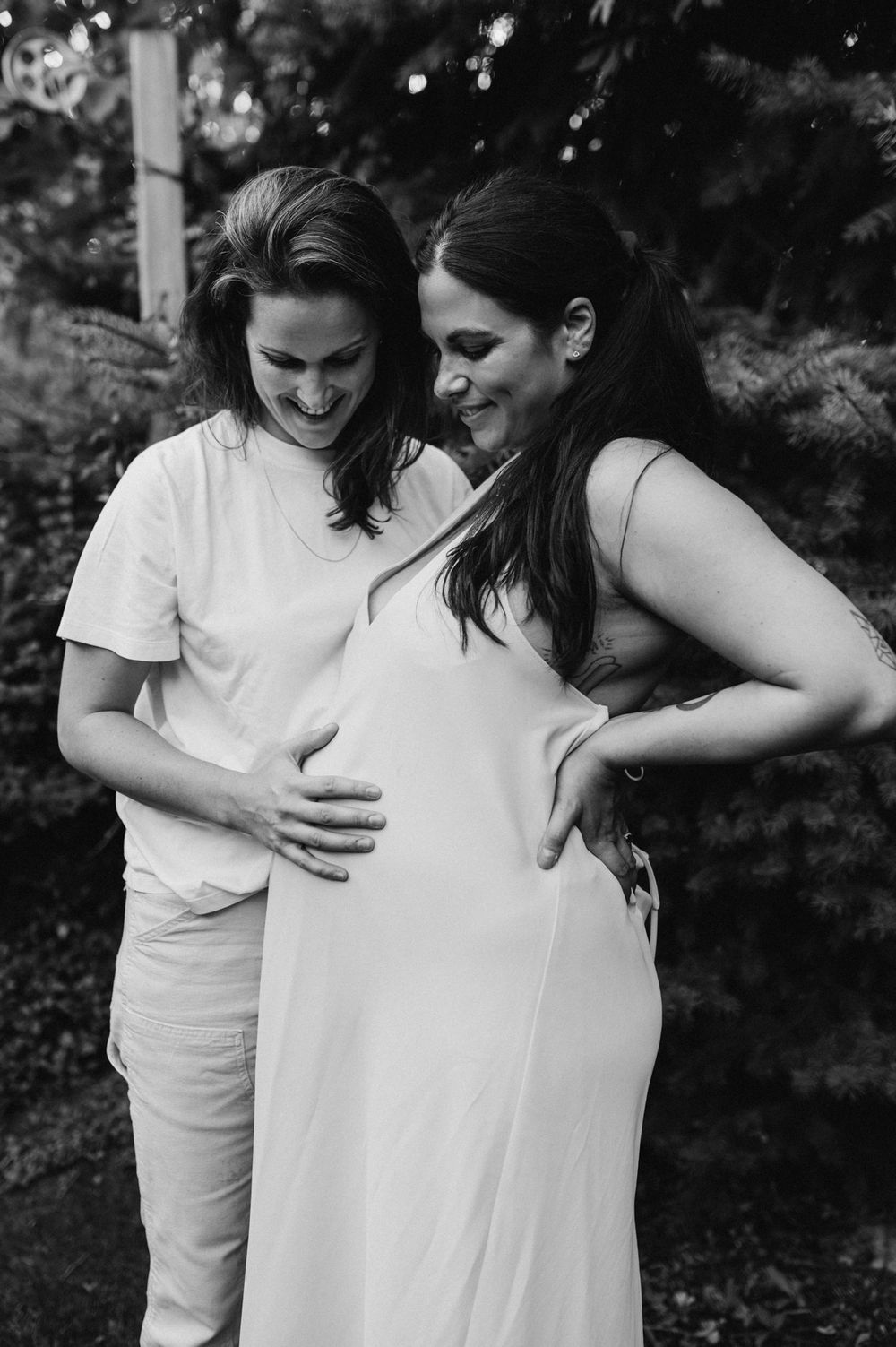 Black and white photo of two smiling women sharing a joyful maternity moment, one touching the pregnant belly.