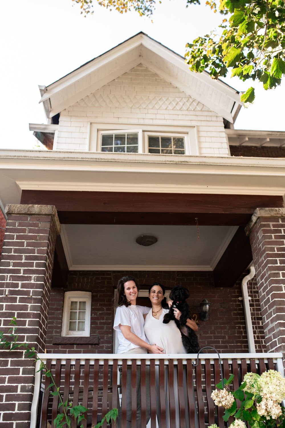 Couple smiling on brick home porch with black dog.