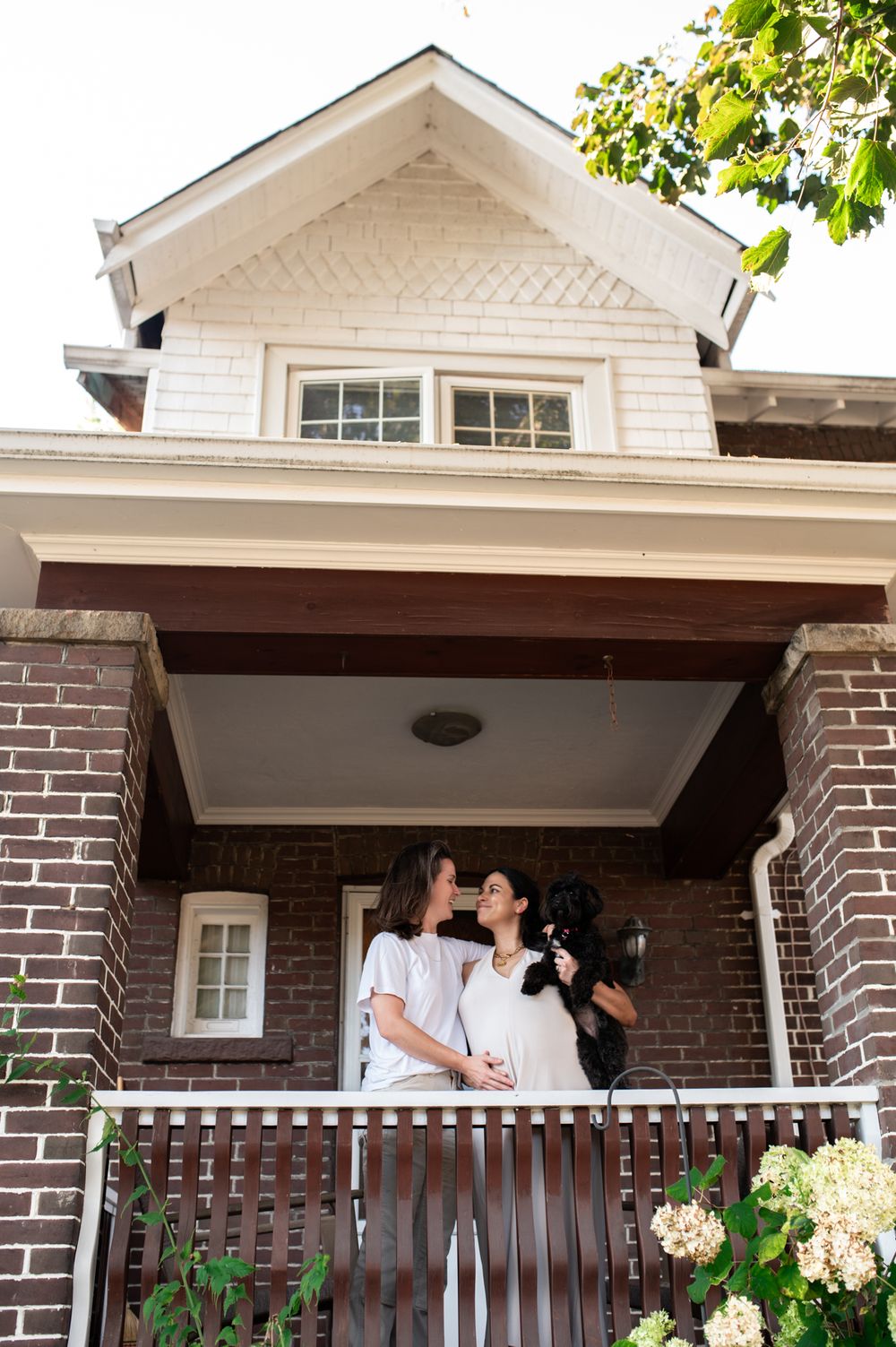 Two women sharing a kiss on a brick home porch with black dog.