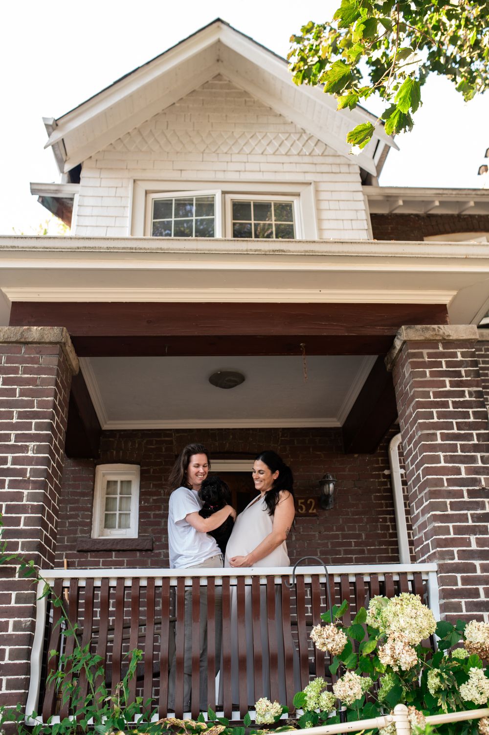 Two women laughing together on a brick house front porch.