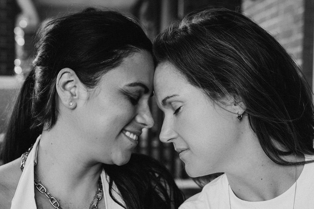 Black and white close-up of two women smiling forehead to forehead.