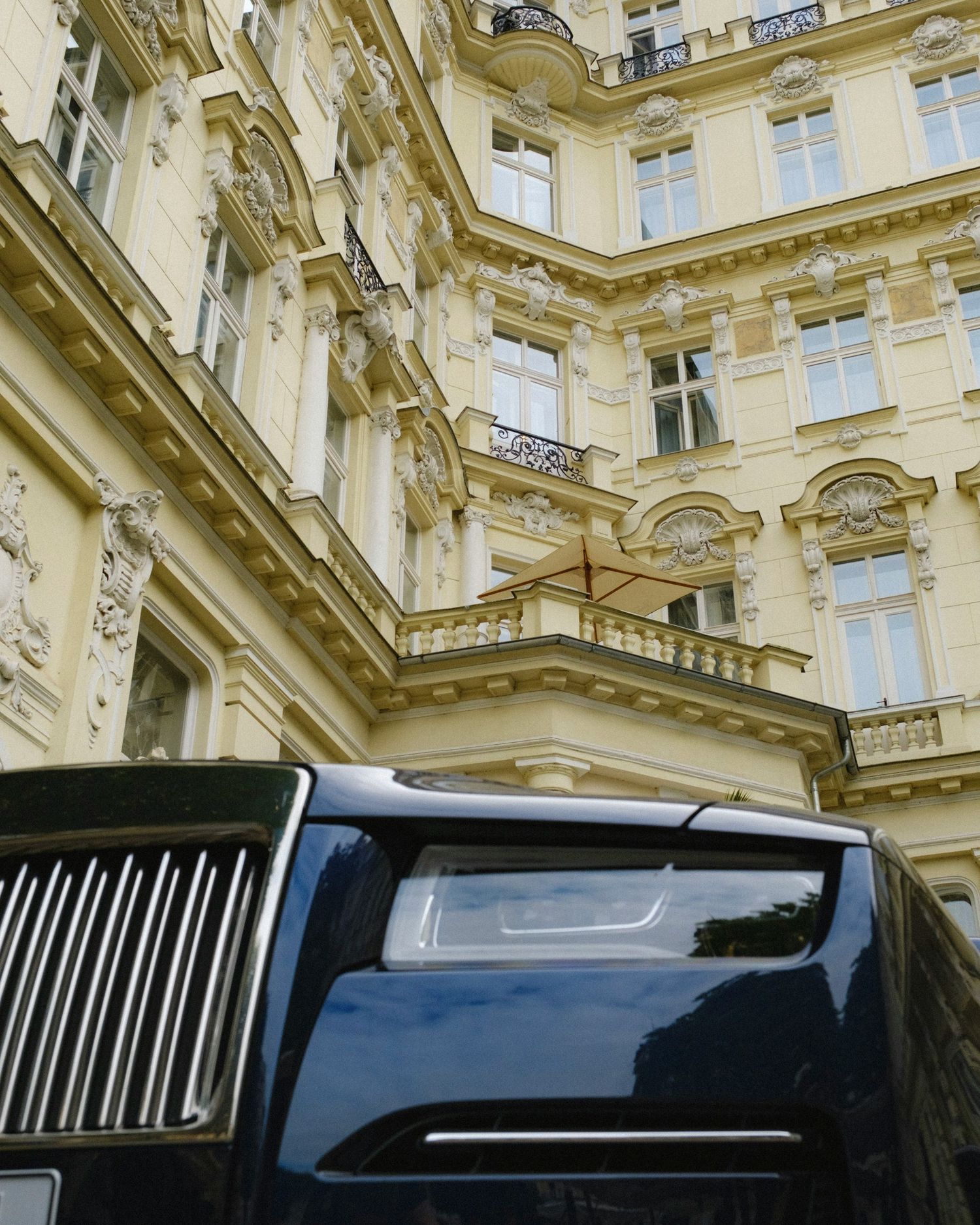 Luxury black Rolls-Royce parked in front of ornate European baroque architecture building with decorative facade.