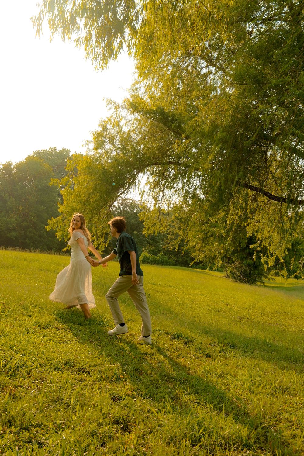 Young couple holding hands running through a sunlit green park at sunset.