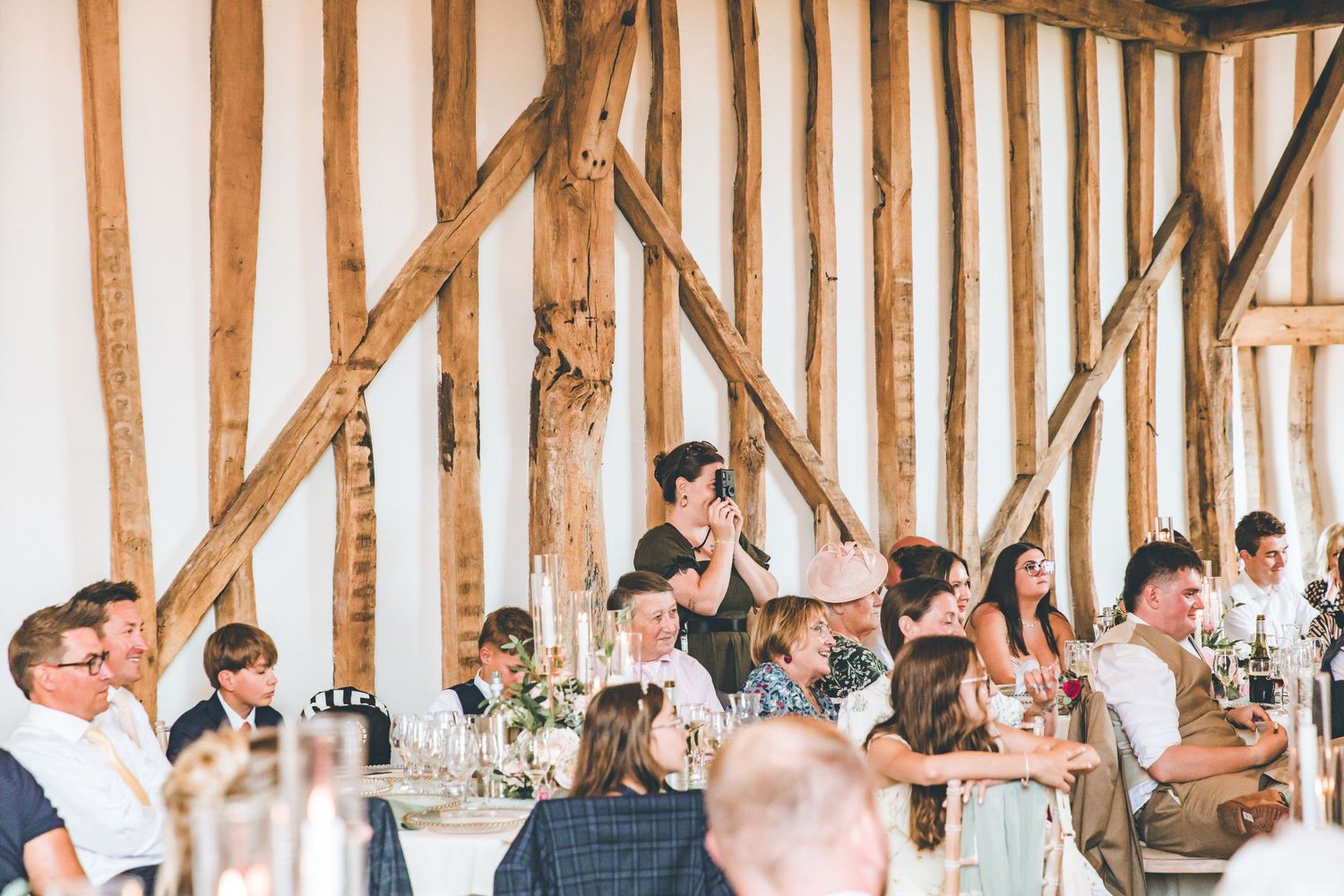 Guests seated at decorated tables in a rustic barn wedding venue with exposed wooden beams and natural light.