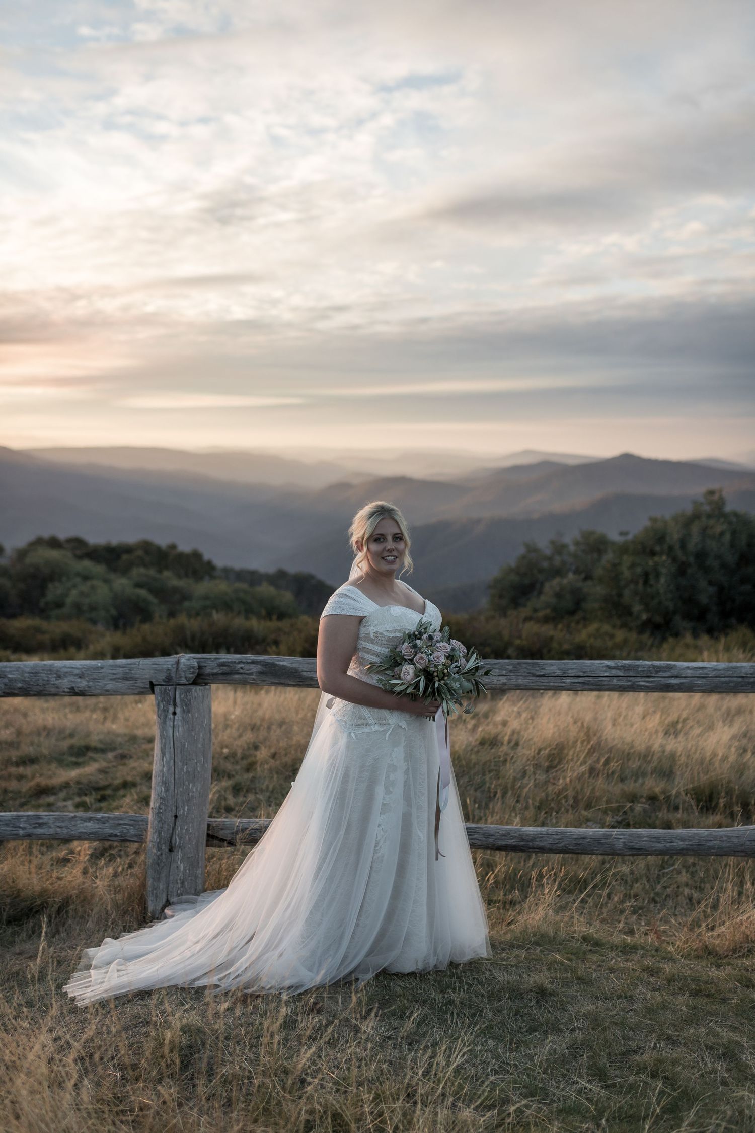 Bride and groom gazing at each other in a sunlit field with a scenic countryside estate backdrop.