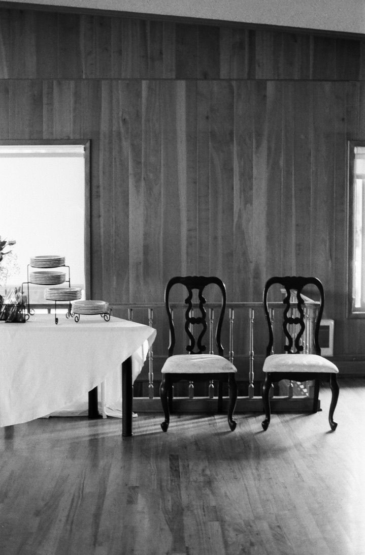 Two ornate Queen Anne chairs beside a cake table against wood-paneled wall in black and white reception venue.