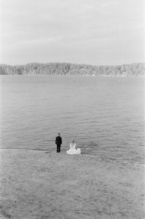 Black and white photo of a bride and groom standing at the shoreline of a vast lake.