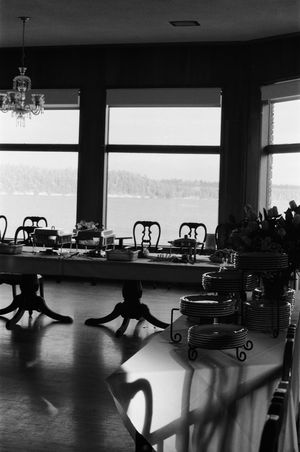 Elegant indoor dining setup with long tables, stacked plates, and lake views through large windows.